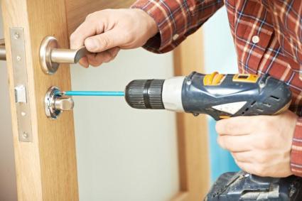 carpenter at lock installation with electric drill into interior wood door